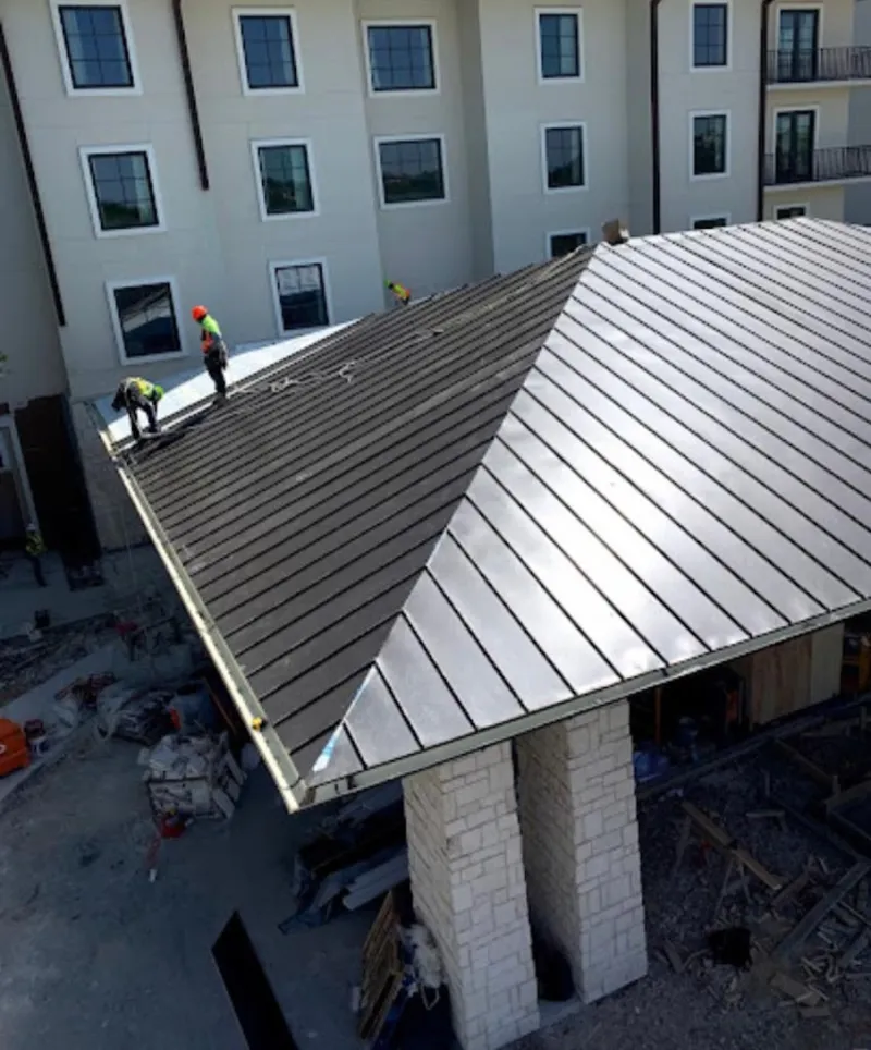 Crew installing standing seam metal roof panels on a commercial project in South Lyon